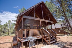 Una baita in legno con veranda, barbecue e una scala che porta all'ingresso.