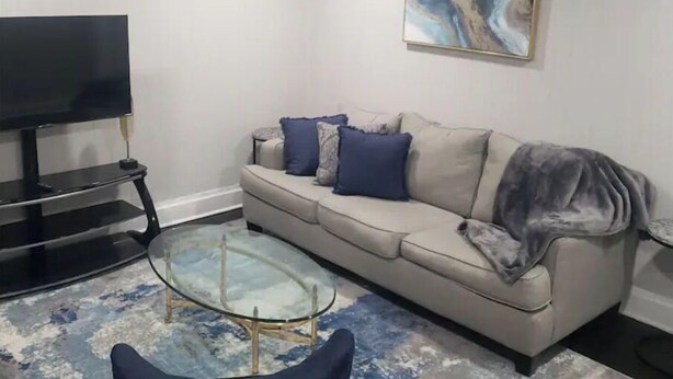 A living room with a beige sofa, a glass coffee table, a flat-screen TV, and a marble-patterned painting on the wall.