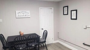 A dining area with a table and four chairs, a white door, and two framed pictures on the wall.