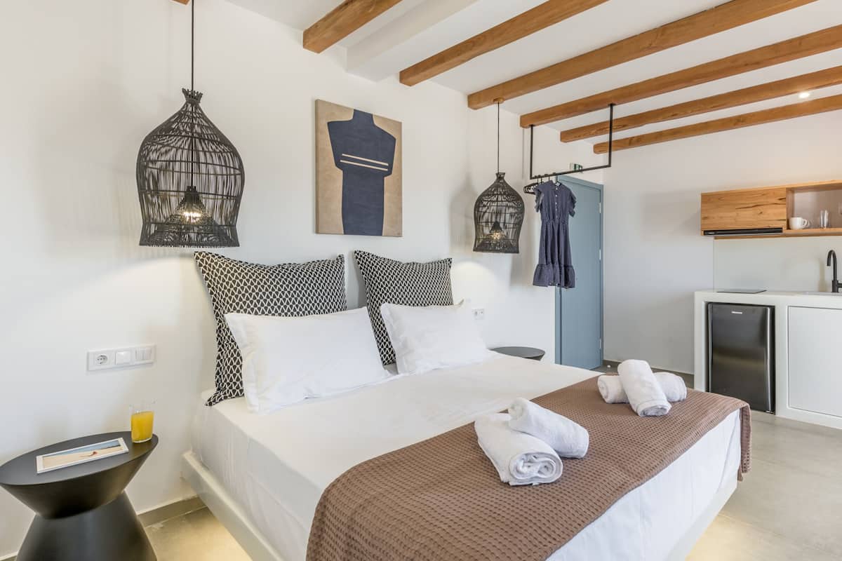 Ein modernes Schlafzimmer mit Bett, Nachttisch und kleinem Schreibtisch. Es gibt eine Küchenzeile mit Mikrowelle, Kaffeemaschine und Spüle.