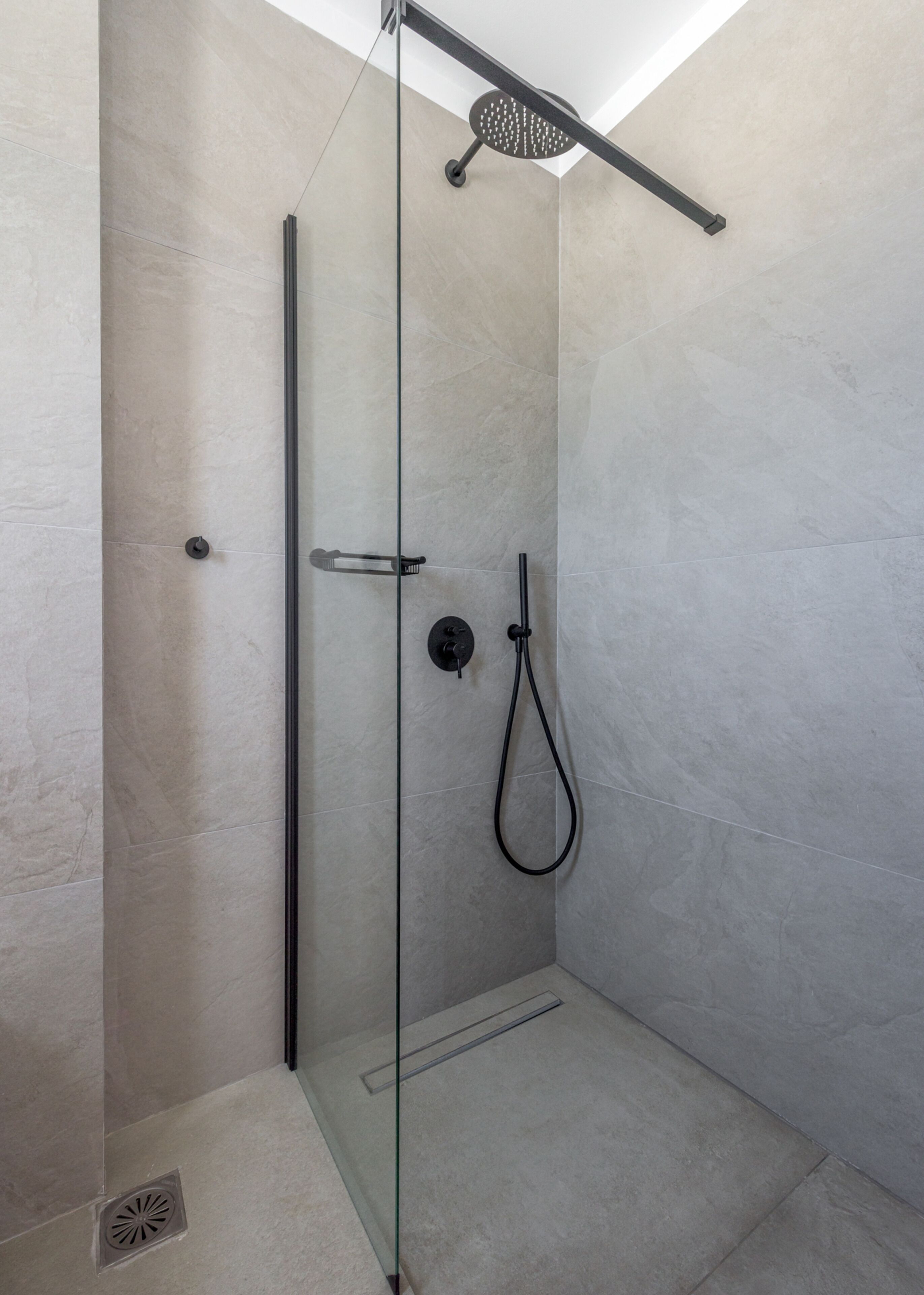 Una ducha moderna con puerta de vidrio, cabezal de ducha de mano y panel de control en la pared.