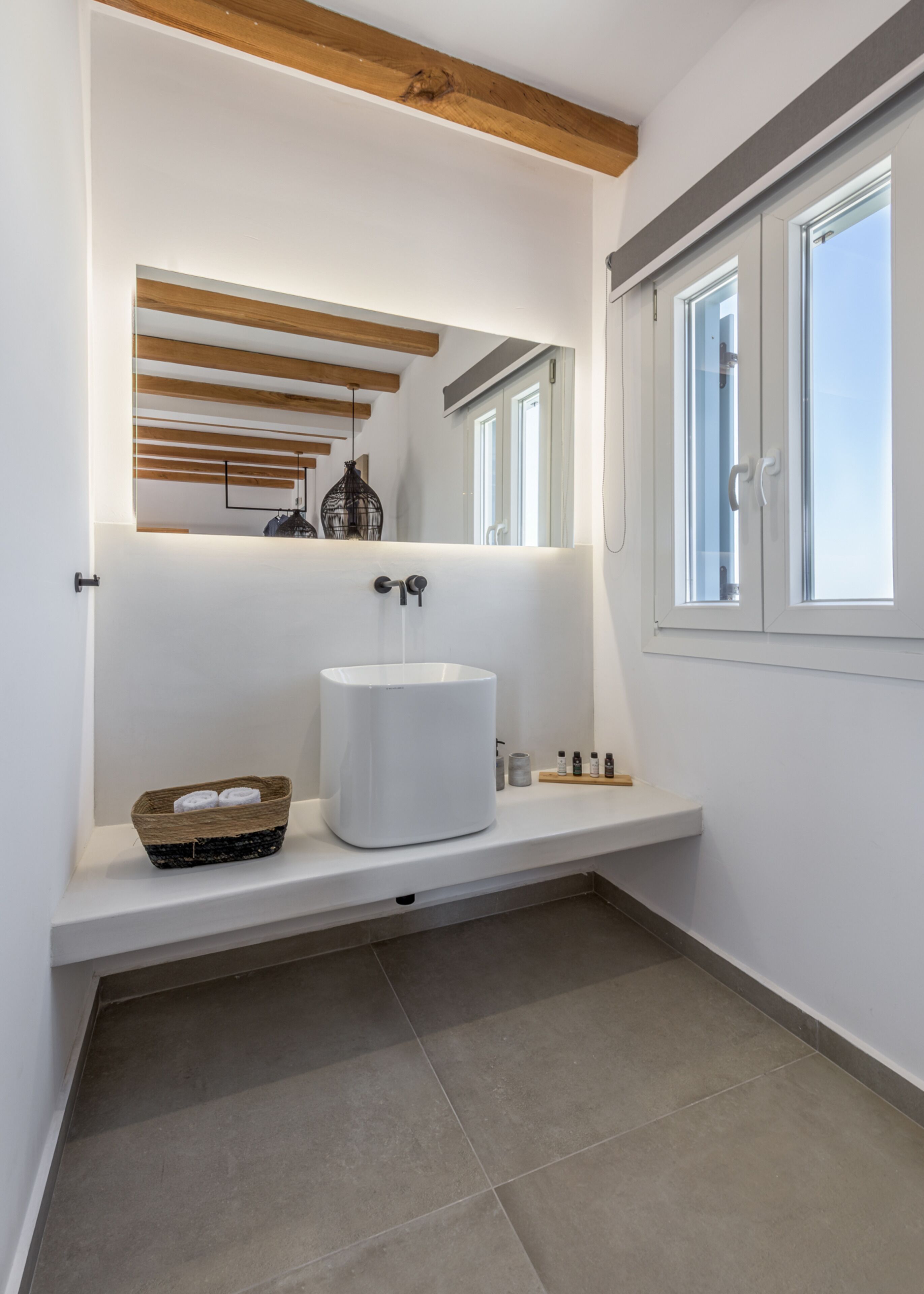 A modern bathroom with a large white sink, wooden beams on the ceiling, and a window with a view.