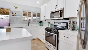 A modern kitchen with white cabinetry, a stove, oven, microwave, and a refrigerator. - Mango Manor - Close to festivals & tennis gardens! (Indio)