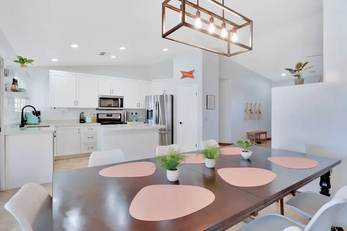 Une cuisine moderne avec des meubles blancs, des appareils en acier inoxydable et un coin repas comprenant une grande table et des chaises.