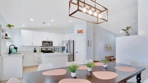 A modern kitchen with white cabinets, stainless steel appliances, and a dining area with a large table and chairs. - Mango Manor - Close to festivals & tennis gardens! (Indio)