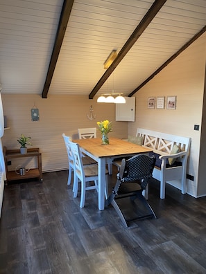 A dining area with a wooden table, white chairs, a bench, and a hanging light fixture. - Cozy idyllic vacation home on the edge of a field 500 m to the Baltic Sea (Neukirchen)