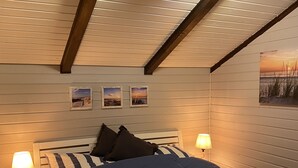 Un dormitori amb un llit, dues tauletes de nit, un ventilador de sostre i tres quadres a la paret.