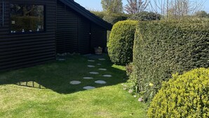 Una cabana de fusta amb una antena parabòlica, un jardí ben cuidat i un camí de pedra que condueix a l'entrada.
