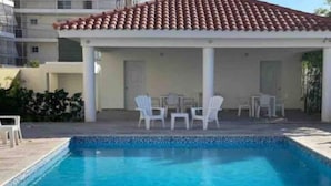 A swimming pool with white chairs and a covered seating area. - Lovely condo with pool near beach (La Romana)