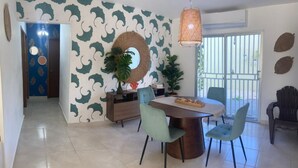 A dining area with a round table, two chairs, a hanging light fixture, and a wall with a leafy pattern. - Lovely condo with pool near beach (La Romana)