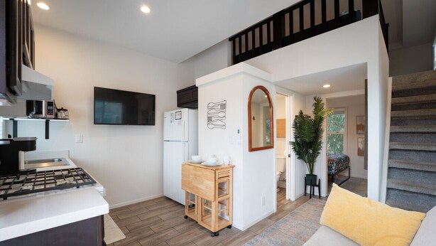 A compact living space with a kitchenette, a sofa with a yellow cushion, and a staircase leading to an upper level.