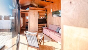 Un interior moderno con techo de madera, estanterías empotradas, sofá rosa y puerta de cristal que da a un espacio exterior.
