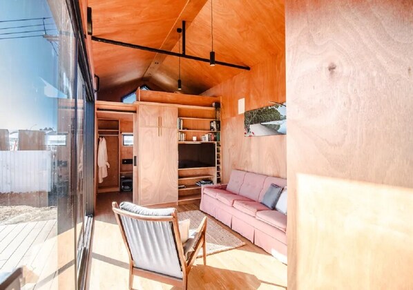 Un interior moderno con techo de madera, estanterías empotradas, sofá rosa y puerta de cristal que da a un espacio exterior.