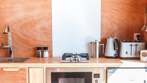 Una cocina compacta con un lavamanos de acero inoxidable, una estufa a gas, un hervidor y un tostador.