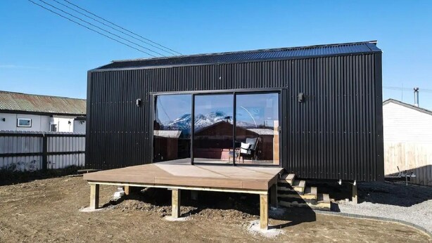 Un edificio moderno de color negro con un amplio ventanal y una terraza de madera al frente.