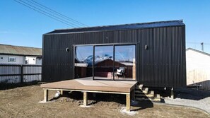 Un edificio moderno de color negro con un amplio ventanal y una terraza de madera al frente.