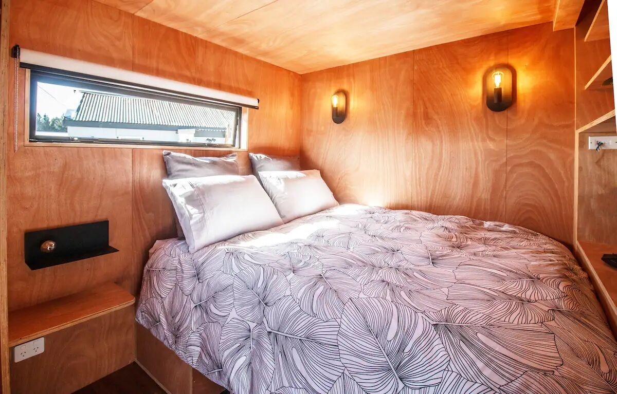 Une chambre à coucher de taille réduite, comprenant un lit, une fenêtre et deux lampes fixées au mur.