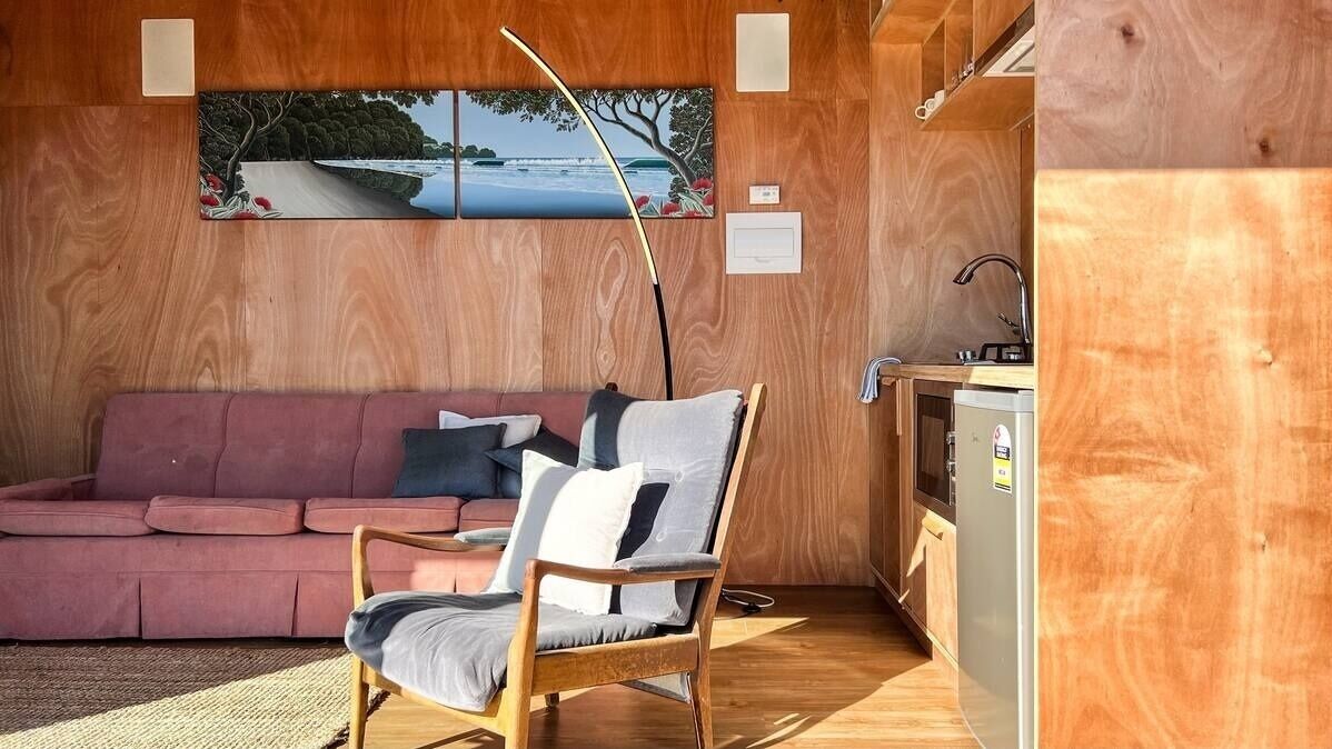 Een gezellige kamer met een houten wand, een roze bank, een houten stoel en een kleine kitchenette.