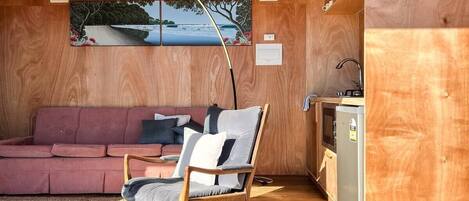 A cozy room with a wooden wall, a pink sofa, a wooden chair, and a small kitchenette.
