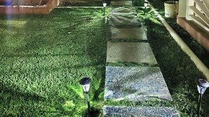 Una vista notturna di una zona residenziale con un prato curato, un vialetto in pietra e un ingresso con cancello.