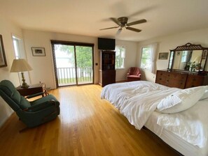 Relax in this serene bedroom with a large bed, ceiling fan, and a view of the outdoors through glass doors.
