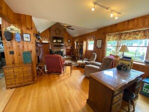 Cozy cabin-style room with a central fireplace, wooden desk, and comfortable seating area.