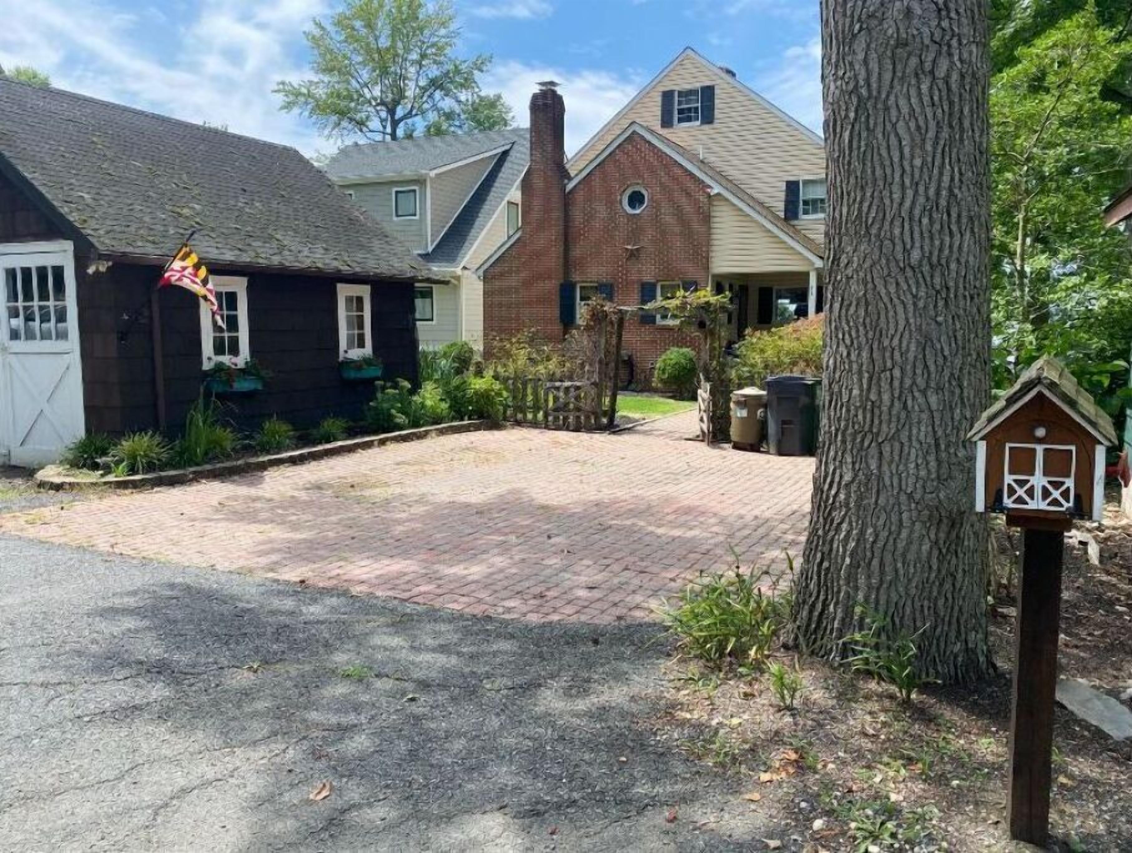 A residential driveway leading to a house with a brick chimney, a wooden fence, and a birdhouse.