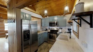 A modern kitchen with stainless steel appliances, light blue cabinets, and wooden beams. - Mountainside cabin with breathtaking views/hot tub/arcade/pet friendly (Pigeon Forge)