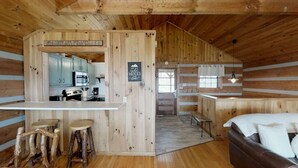 A rustic cabin interior with a kitchen, dining area, and a cozy bed. - Mountainside cabin with breathtaking views/hot tub/arcade/pet friendly (Pigeon Forge)