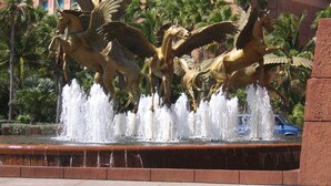 A fountain with golden horse statues and water jets, surrounded by palm trees and a building with balconies in the background. - Harborside Resort @ Atlantis 2 BR Sleep 6-8 (Nassau)