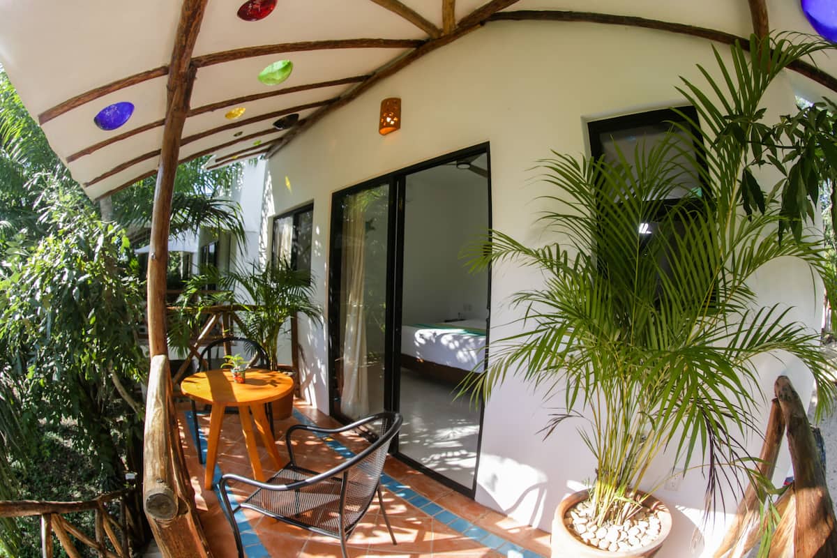 A covered patio with a round table and chairs, a potted plant, and a sliding glass door leading to a bedroom.