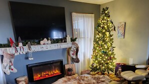 Un salón acogedor con chimenea, un árbol de Navidad y un televisor montado en la pared.