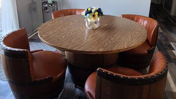 Une table de salle à manger ronde en bois, entourée de six chaises en cuir, un vase contenant des plantes séchées et un tableau accroché au mur.