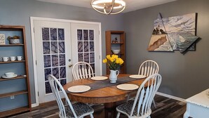 Un comedor con mesa de madera, sillas blancas y un jarrón de flores amarillas.