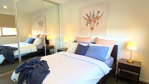 A hotel room with a large bed, two bedside tables with lamps, a mirror, and a wall-mounted artwork. - StayCentral-Heidelberg Heights Penthouse (Heidelberg Heights)