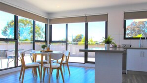 A modern kitchen with large windows, a dining area with chairs, and a small island. - StayCentral-Heidelberg Heights Penthouse (Heidelberg Heights)