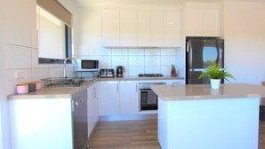 A modern kitchen with white cabinets, stainless steel appliances, and a central island. - StayCentral-Heidelberg Heights Penthouse (Heidelberg Heights)