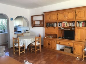 A compact kitchen with wooden cabinets, a dining table with chairs, and a built-in TV.
