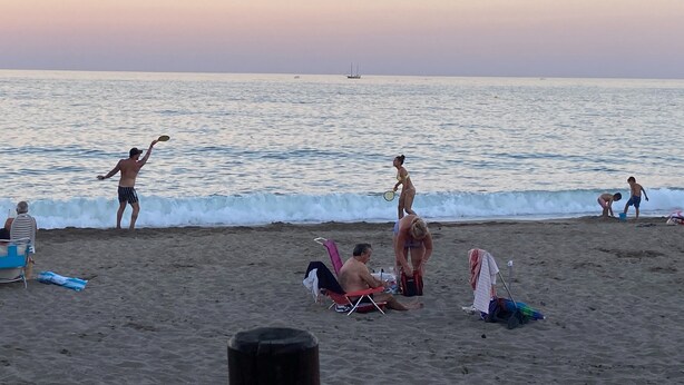 Eine Strandansicht mit Menschen, die verschiedene Aktivitäten ausüben, darunter Frisbee spielen und ein Paddel benutzen.
