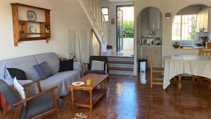 Ein gemütliches Wohnzimmer mit einer Couch, einem Couchtisch und einem Esstisch für zwei Personen. Eine Treppe führt zu einem offenen Bereich, durch einen Bogen ist eine Küche sichtbar.