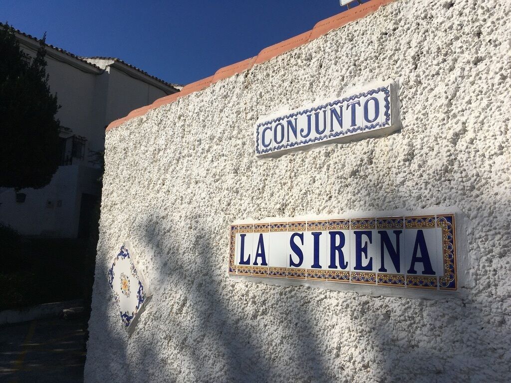 A street sign with "CONJUNTO" and "LA SIRENA" on a textured wall.