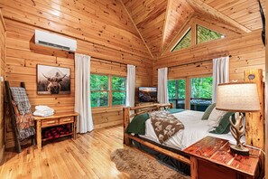 A wooden cabin bedroom with a bed, a TV, a lamp, and a window with curtains.