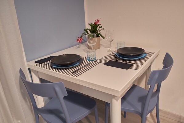 Une table à manger dressée avec des assiettes, des couverts et des verres, entourée de chaises bleues.
