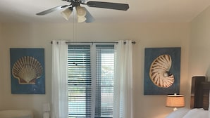 Ein Schlafzimmer mit einem Bett, einem Nachttisch, einer Lampe, einem Deckenventilator und zwei Wandbildern.