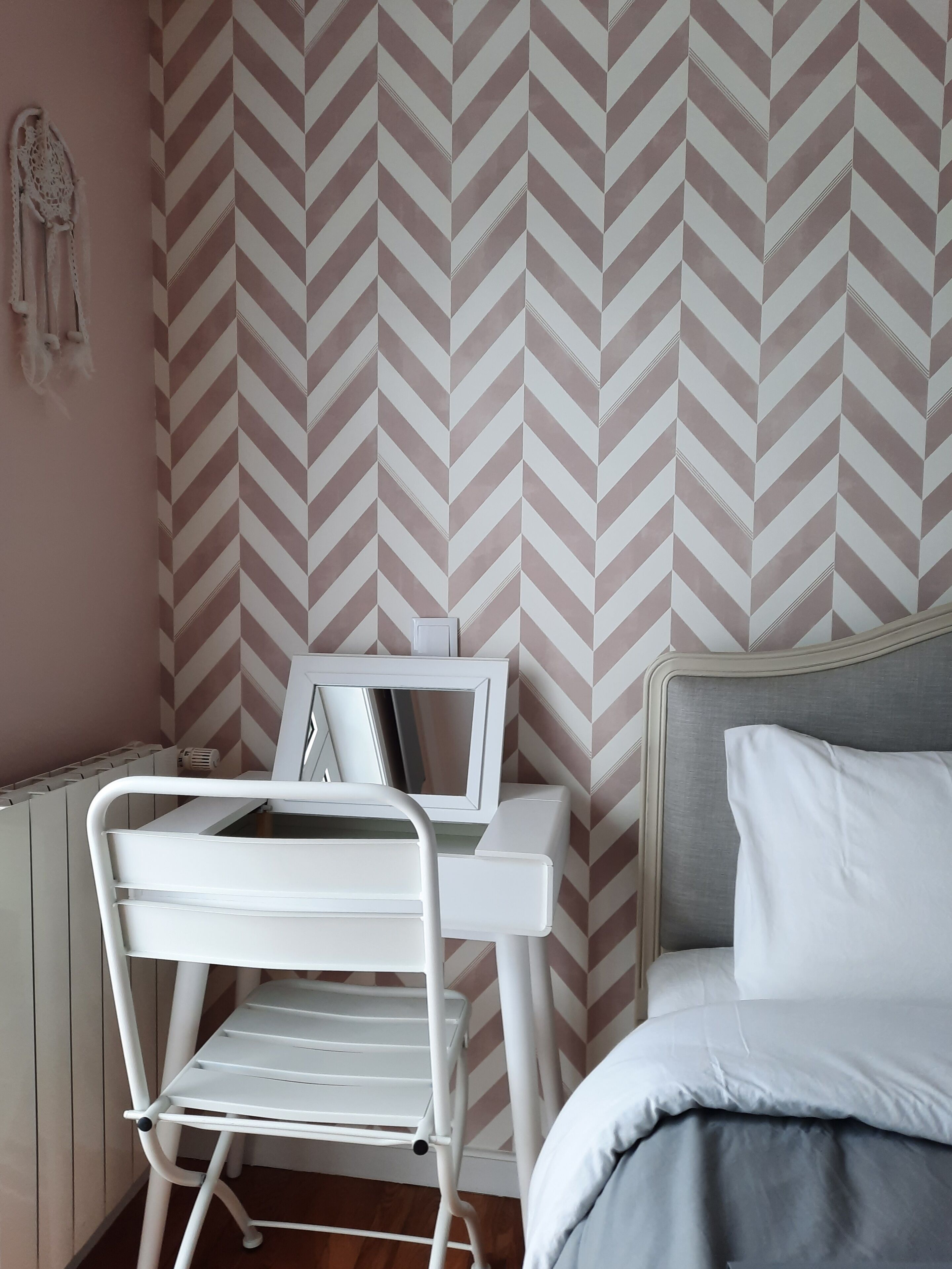 A bedroom with a bed, a bedside table, a chair, and a wall with a chevron pattern.