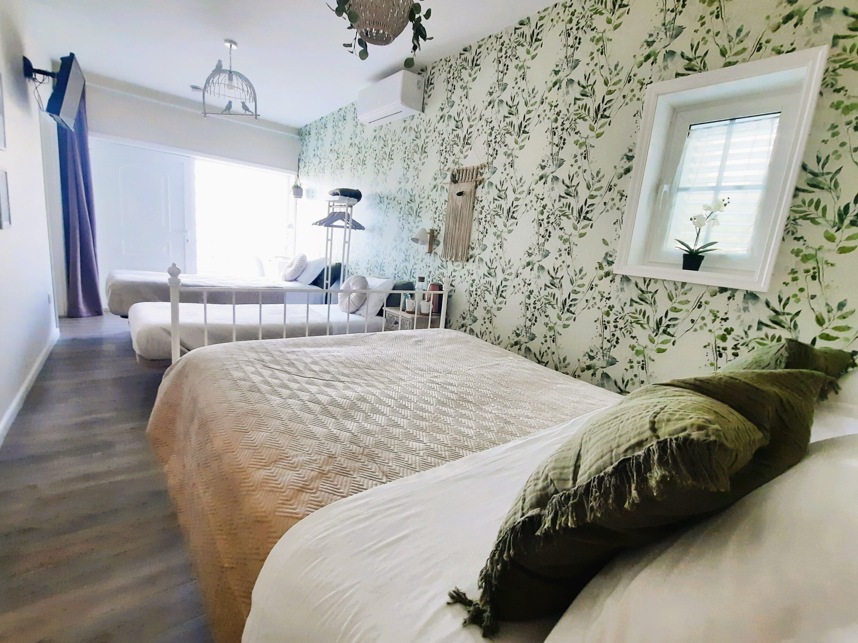 Un dormitorio con una cama grande, una cama más pequeña, una ventana con una planta y un ventilador de techo.