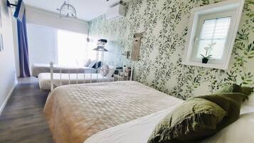 Un dormitorio con una cama grande, una cama más pequeña, una ventana con una planta y un ventilador de techo.