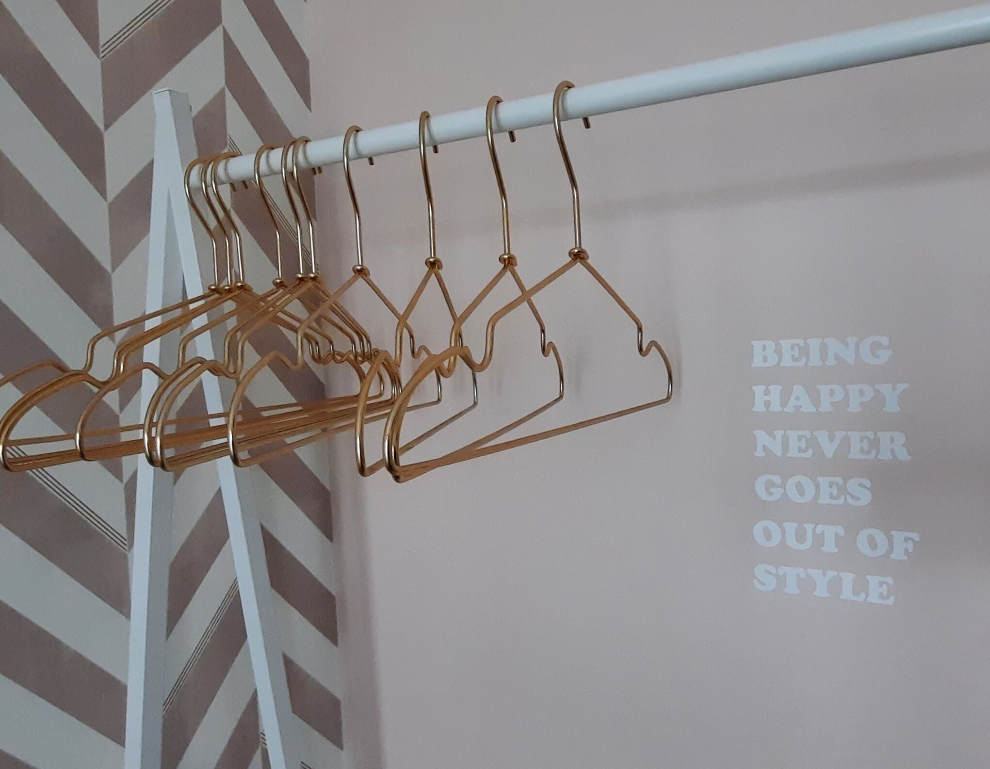 Un perchero con múltiples perchas frente a una pared con un estampado en zigzag y una frase motivacional.