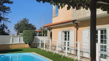 Enjoy a refreshing swim in the pool surrounded by a lush lawn and shaded by a pergola.