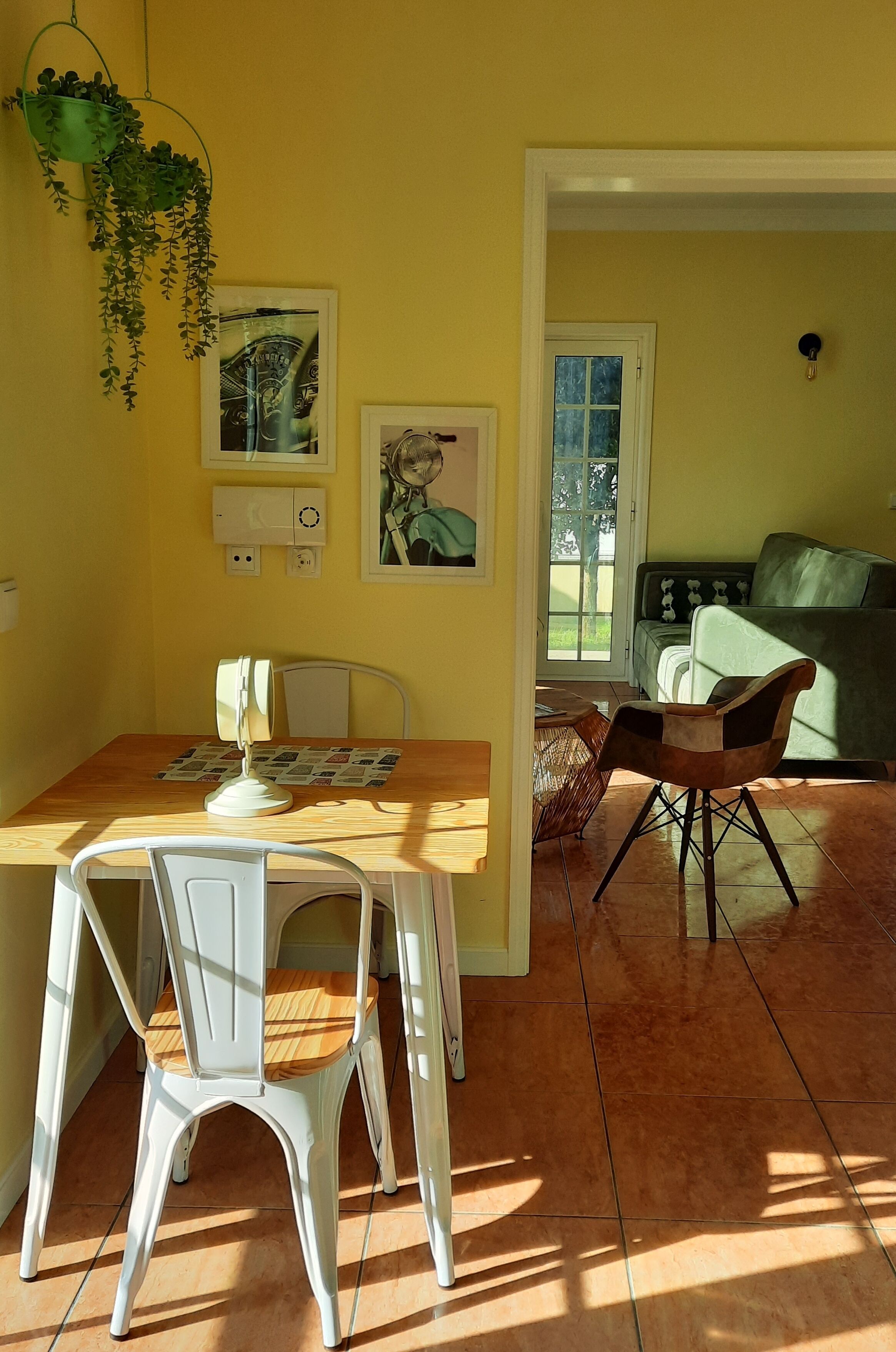 Een eethoek met een houten tafel, witte stoelen, een hangplant en een groene bank op de achtergrond.